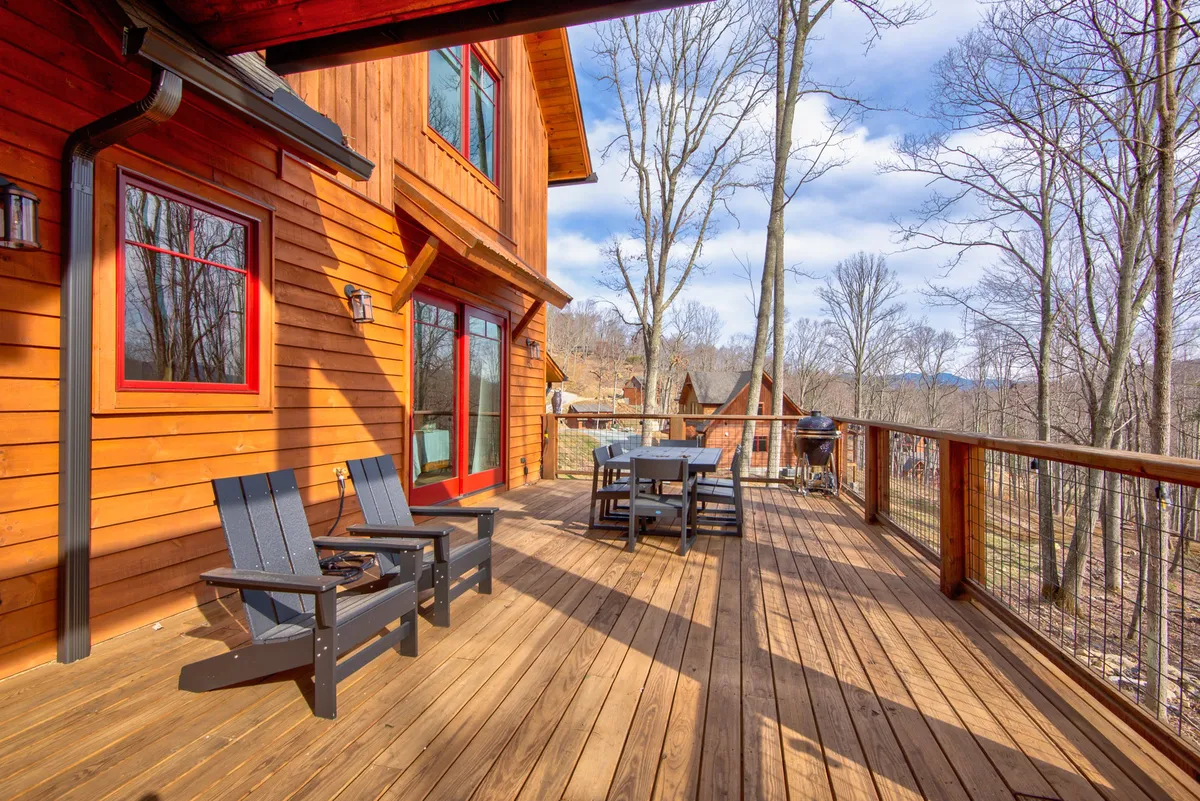 A tranquil wooden deck with outdoor seating, surrounded by trees and featuring a mountain view. The space is ideal for entertaining, enjoying nature, or sharing a meal together outdoors. The relaxed mood suggests a welcoming environment for families to gather, play, or simply soak in the mountain air.