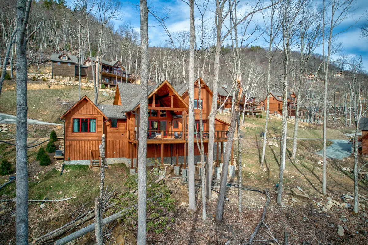 Clusters of wooden cabins nestled among tall trees in a natural mountain landscape. The area is clearly designed for group gatherings and family retreats, with open space for children to play and adults to relax. The mood is cozy and relaxed, inviting exploration and outdoor games.