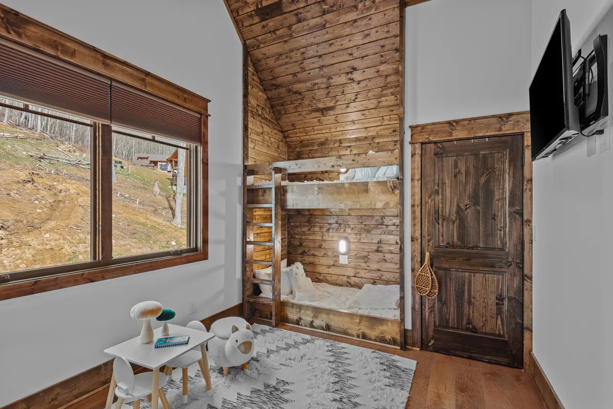 A playful, family-friendly bunk bedroom with a large window, a cozy bunk bed, and a small children's table with chairs on a textured rug, creating a welcoming space for younger guests to rest or play.