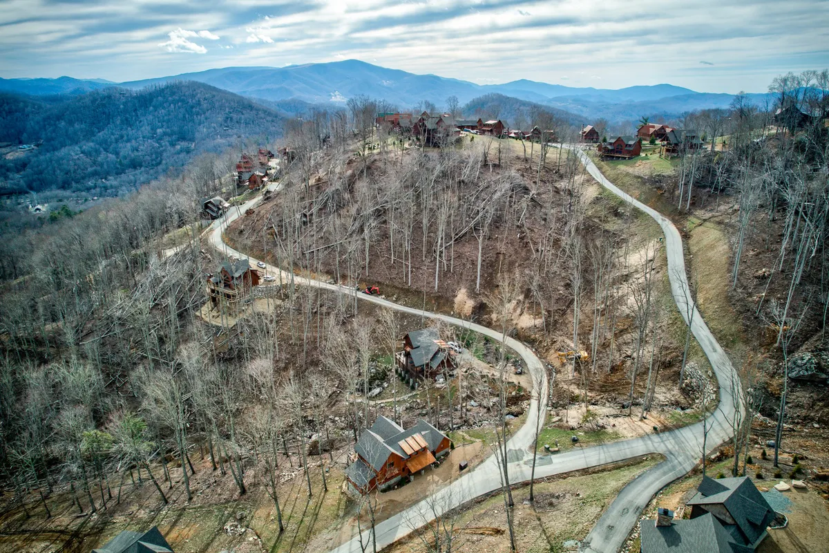This image captures a winding road unfolding through a mountainous landscape, dotted with scattered cabins and bordered by bare trees. The view suggests tranquility and seclusion, with the natural setting offering breathtaking sunrise and stargazing opportunities.