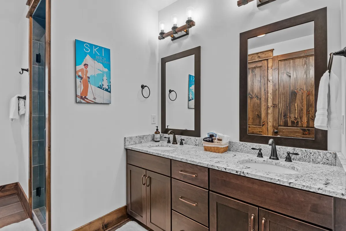 A stylish bathroom scene featuring a double vanity with granite countertops, framed mirrors, and ski-themed artwork. Wooden cabinetry and modern lighting offer both elegance and comfort, perfect for morning routines or unwinding after a day of adventure.