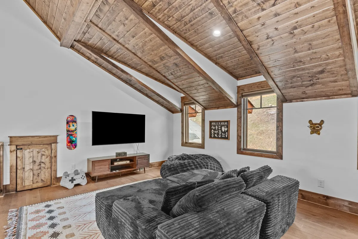 A cozy living area with a large, plush sectional sofa facing a wall-mounted flat-screen TV. The wooden beam ceiling adds rustic character, and decorative wall art provides a stylish accent. The atmosphere is relaxed and inviting, ideal for movie nights or group conversations after a day of adventure.