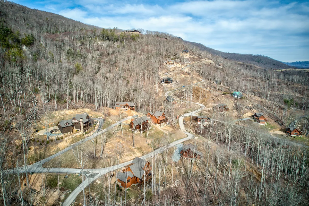 An inviting exterior shot of wooden cabins against a dramatic mountain backdrop, with winding roads and open skies above. Seasonal foliage hints at the changing outdoor activities available throughout the year.